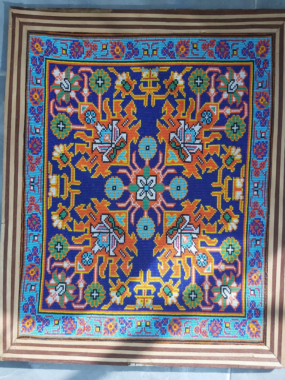 Handmade bead artwork in a striped wooden frame: orange and yellow branches and white, green and turquoise flowers on a deep cobalt-blue field, inside a light turquoise floral border.